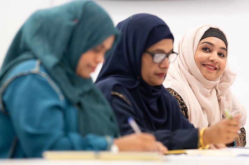 Three women in headscarves write at a desk