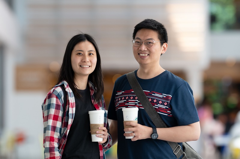 Two young adults holding coffees smile for a photograph