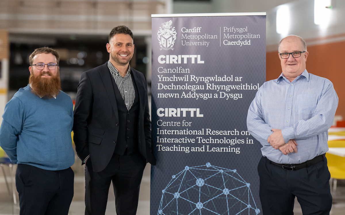 Three members of staff for the Centre for International Research in Interactive Technologies for Teaching and Learning stand either side of an information display