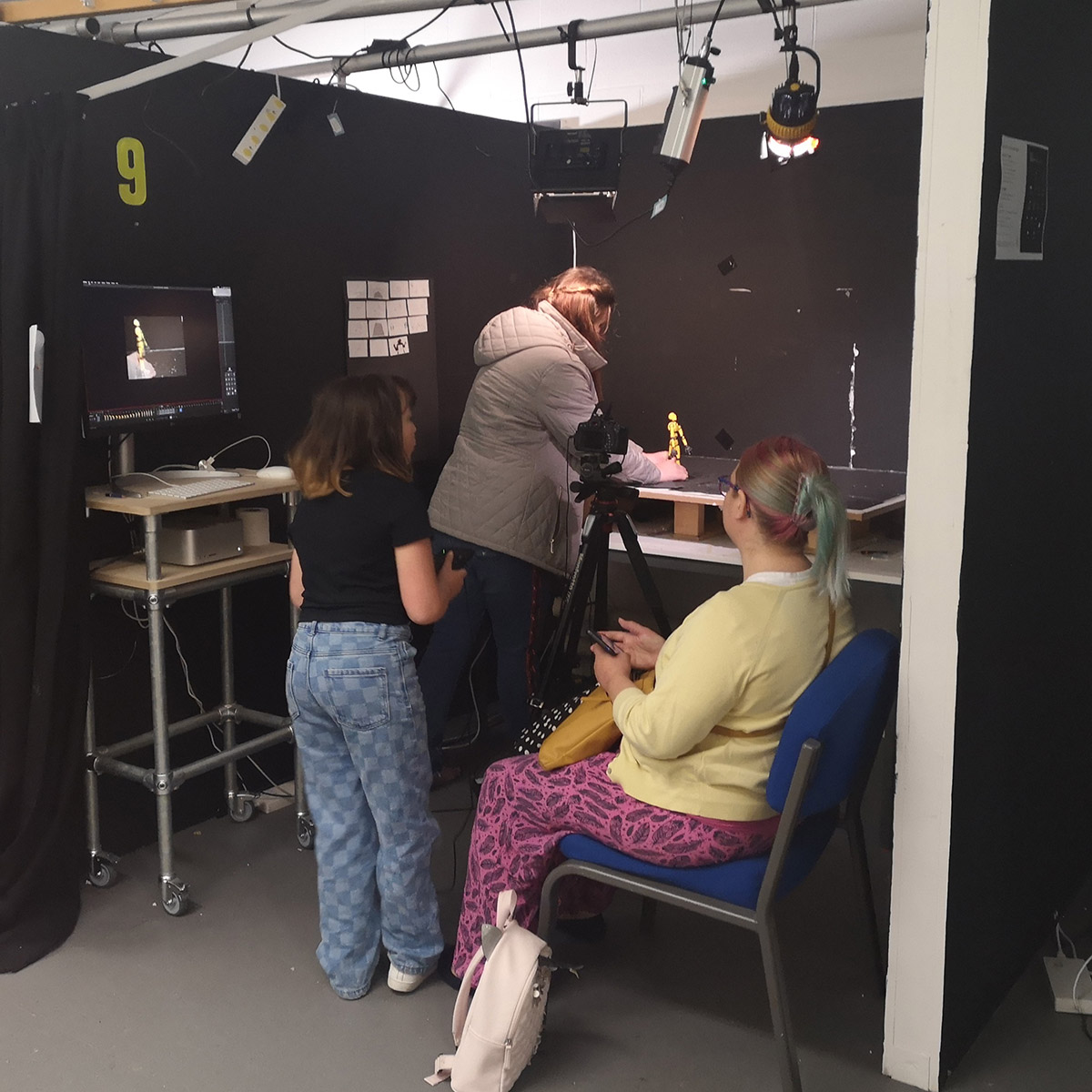 A diverse group of people in a room, engaged in conversation with a camera set up for photography.