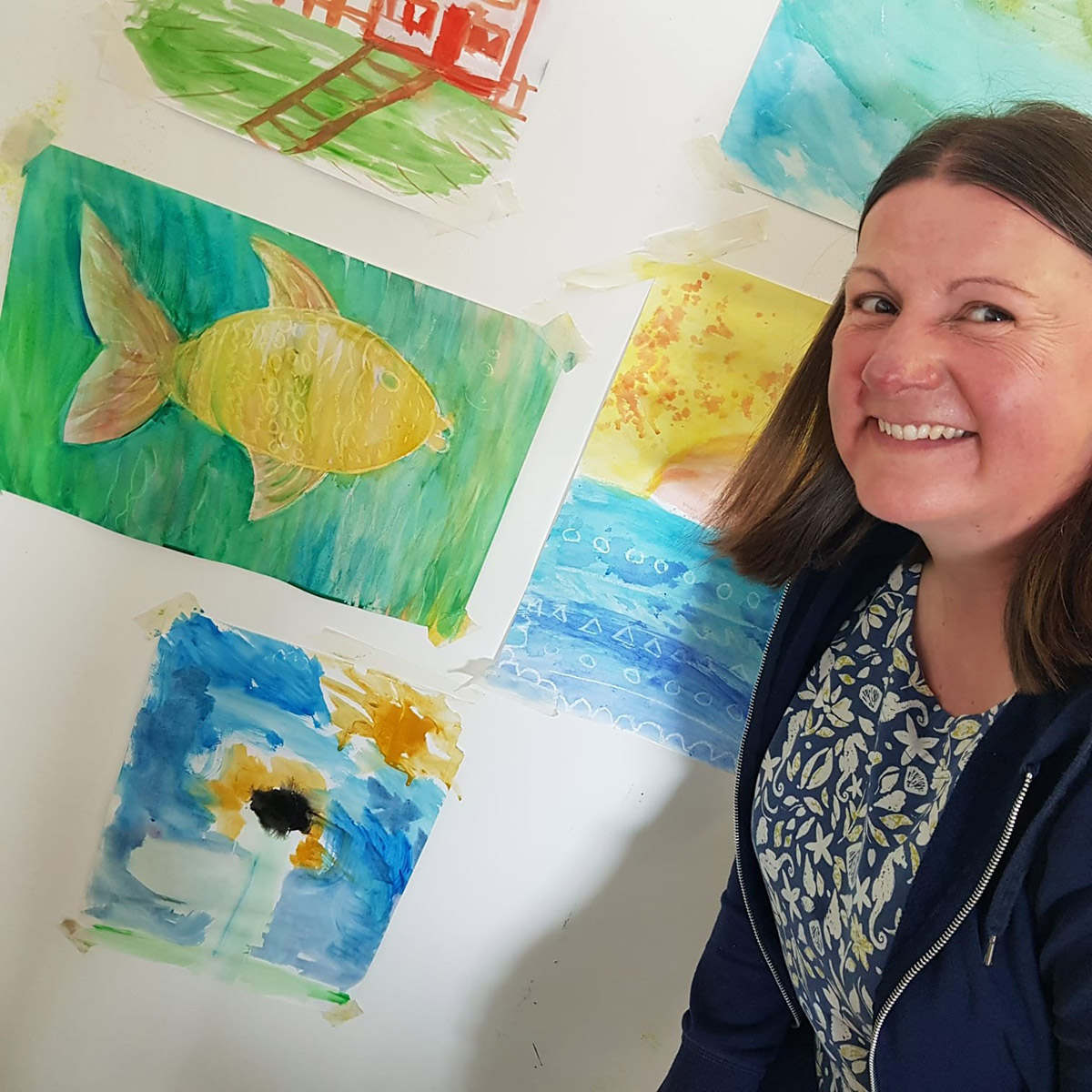 A smiling woman stands before a vibrant wall adorned with an array of paintings.