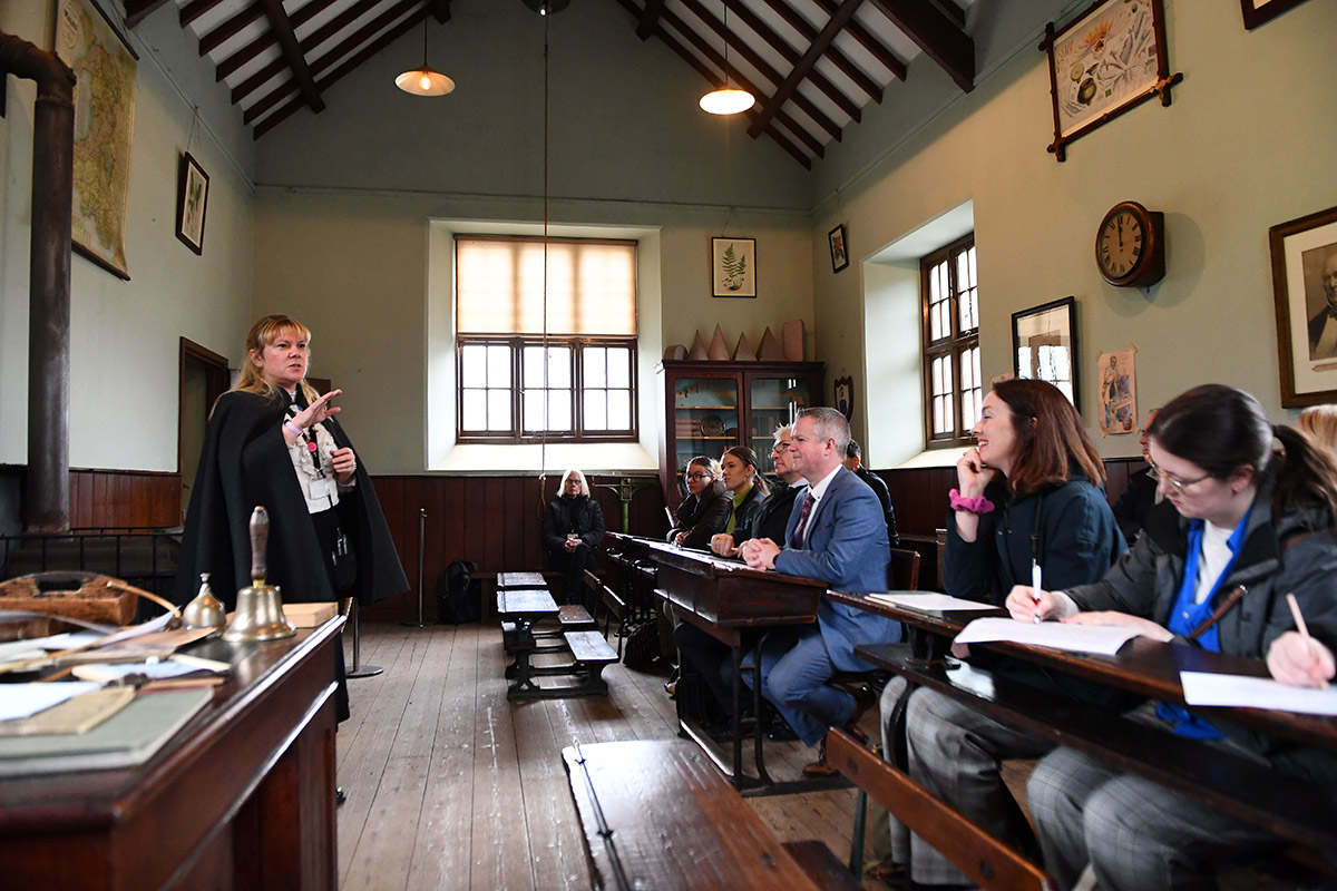 Lecturer speaking to group of attendees in victorian classroom setting.