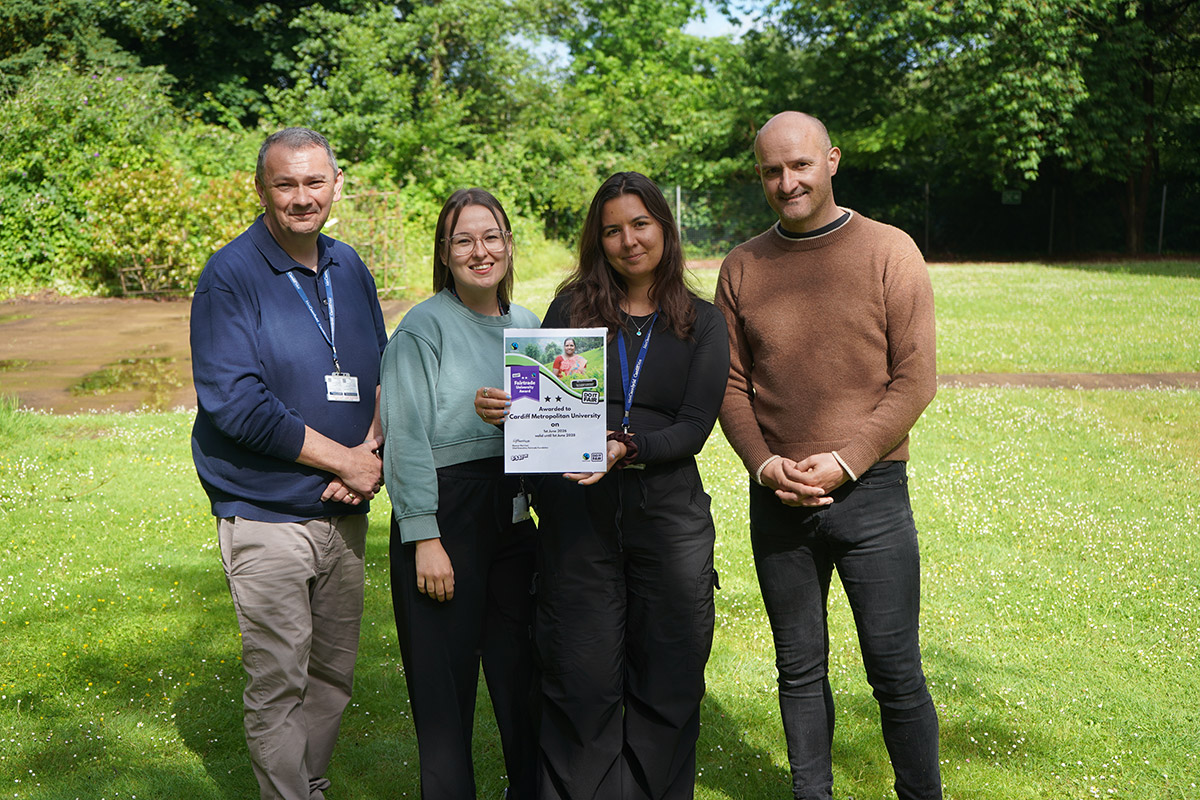 n a park, four people hold a certificate, smiling and celebrating their achievement together.