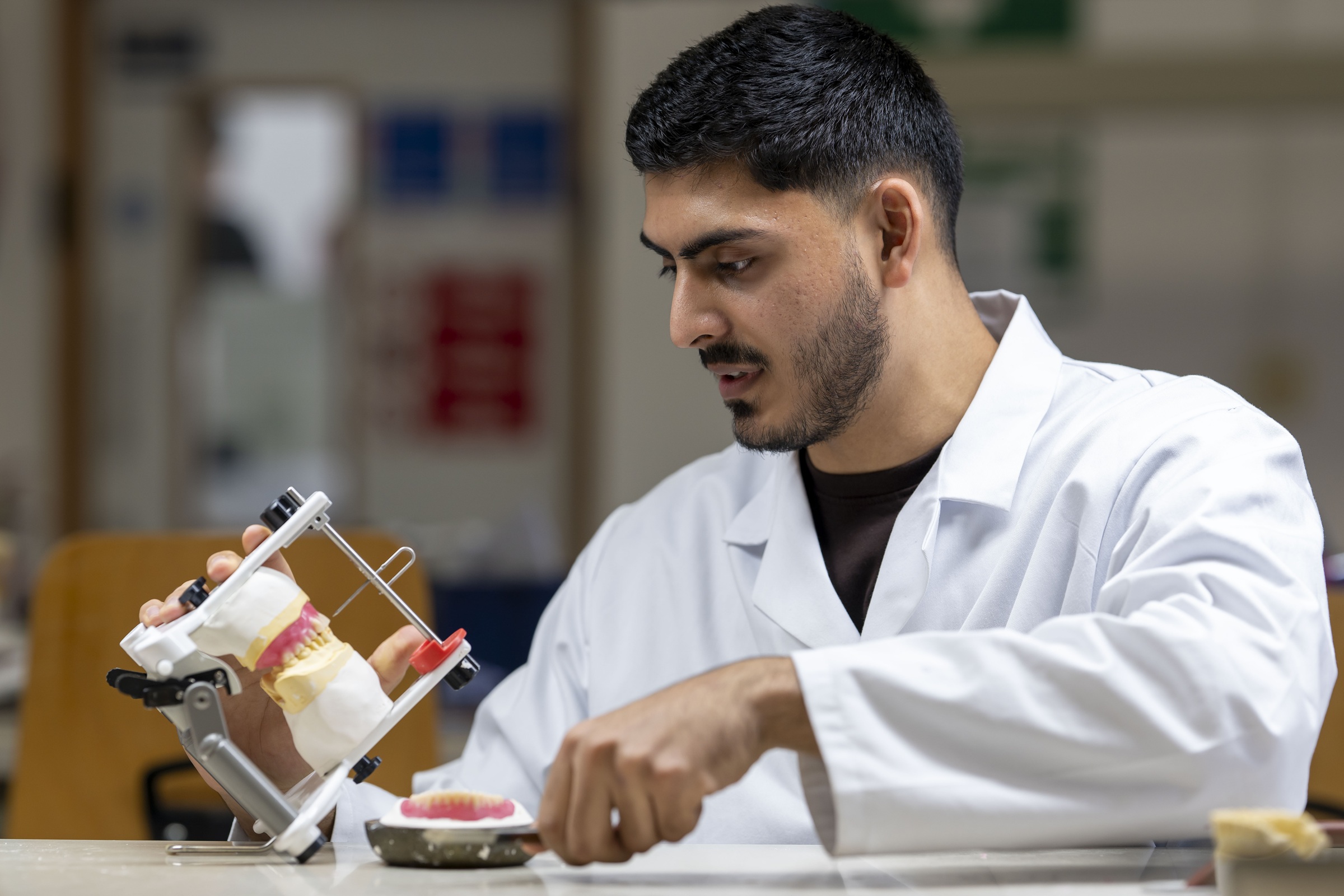 A dental technician works on a set of fake teeth in a mould