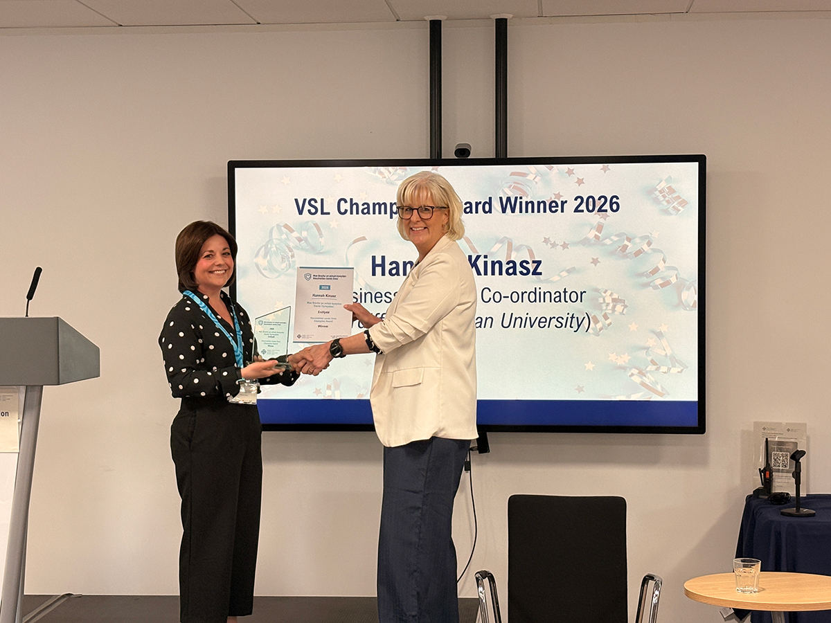 Hannah Kinasz recieving an award from a collegue in front of large monitor