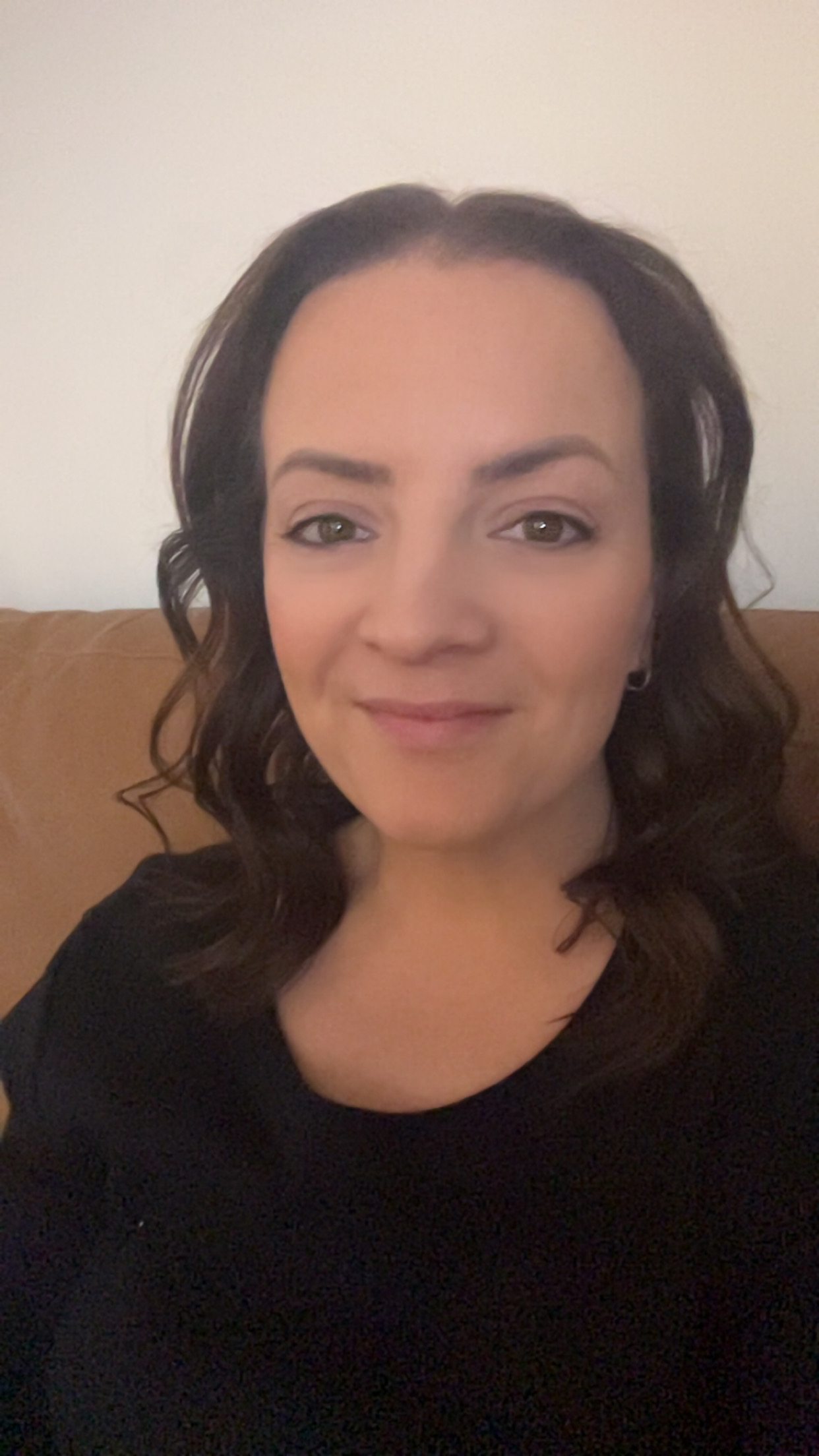 A woman with long hair seated on a couch, exuding a calm and inviting presence in a warm indoor environment.