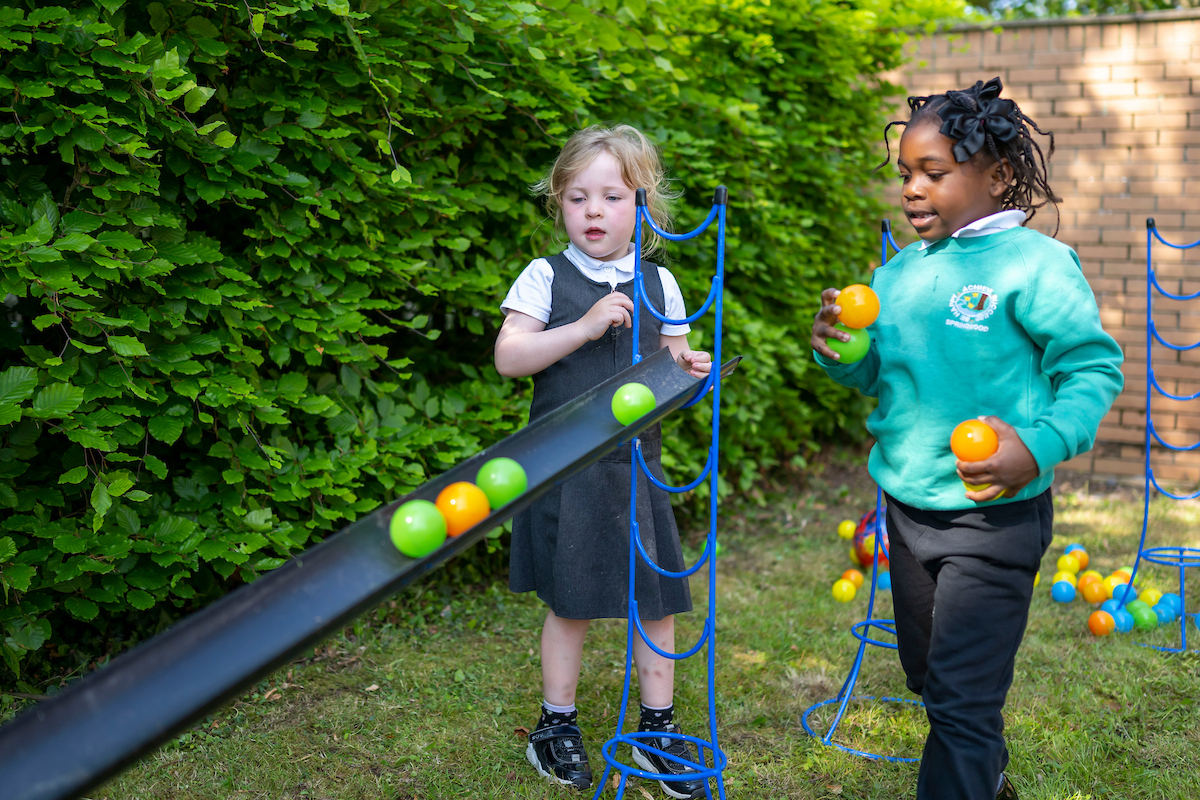 Two kids happily tossing balls back and forth in a sunny yard filled with green grass.