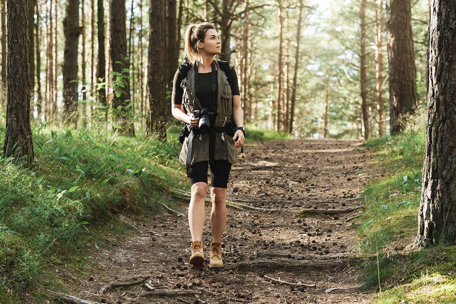 A woman walking through a forest. She is wearing walking gear and carrying a camera.