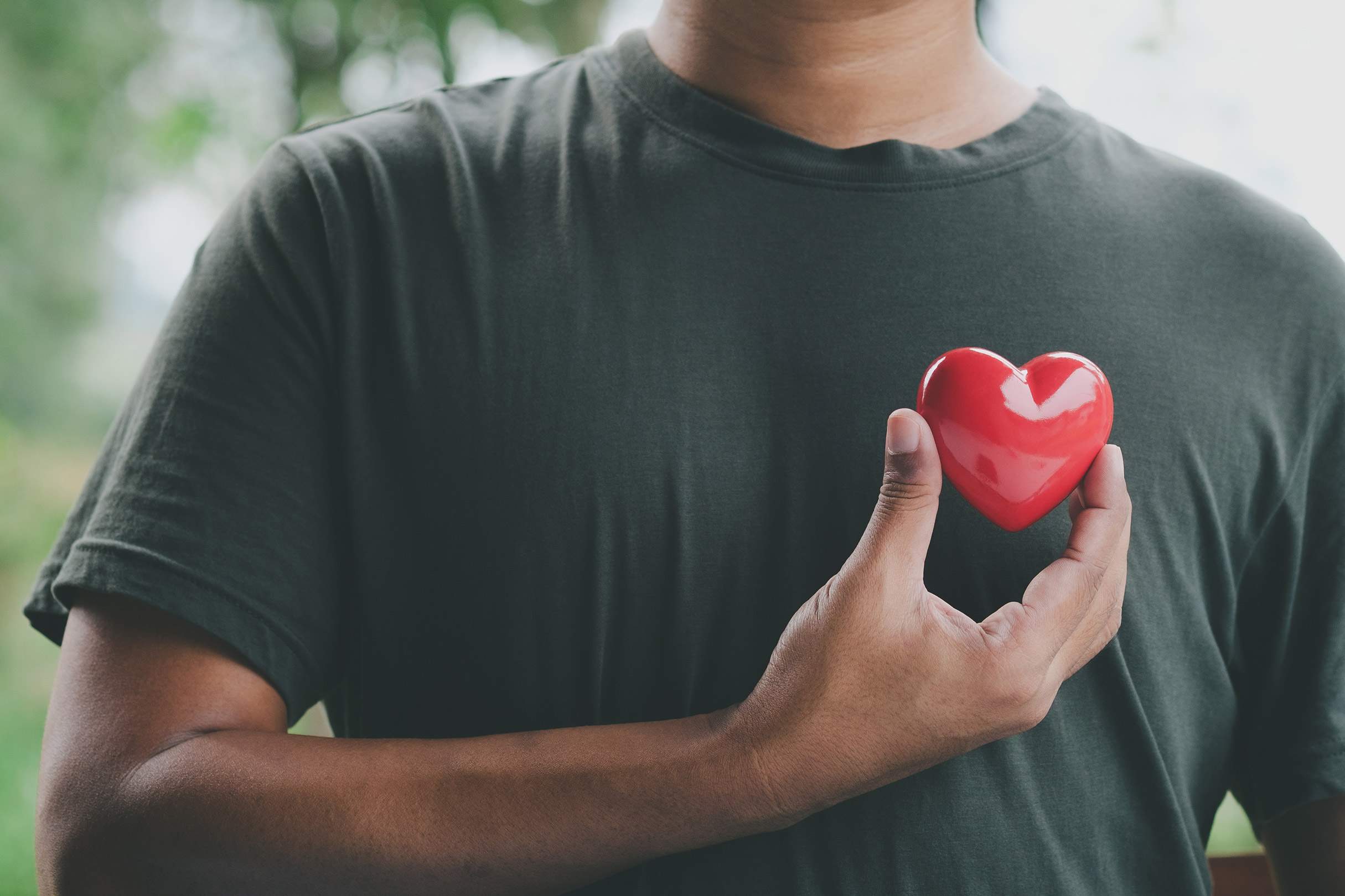 A man holding a small red heart against his chest.