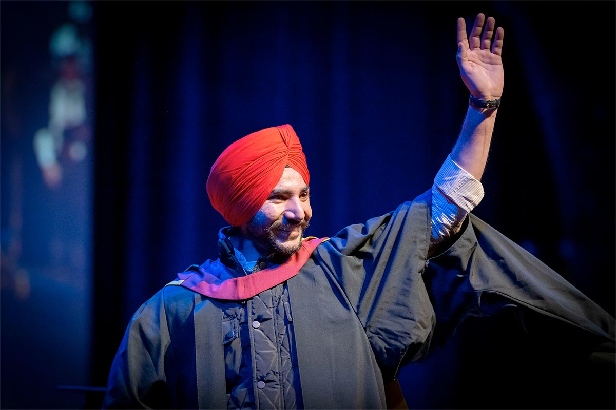 A graduate wearing a red turban and academic gown waves to the audience during the Cardiff Met graduation ceremony.