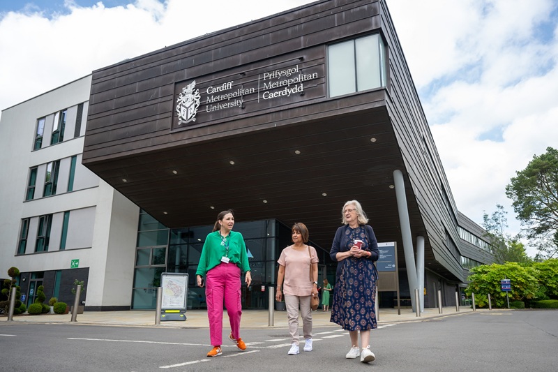 Three adults walk through the campus in front of the Cardiff School of Management building