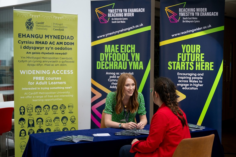 Widening Access staff member speaks to a member of the public in front of a large information stand