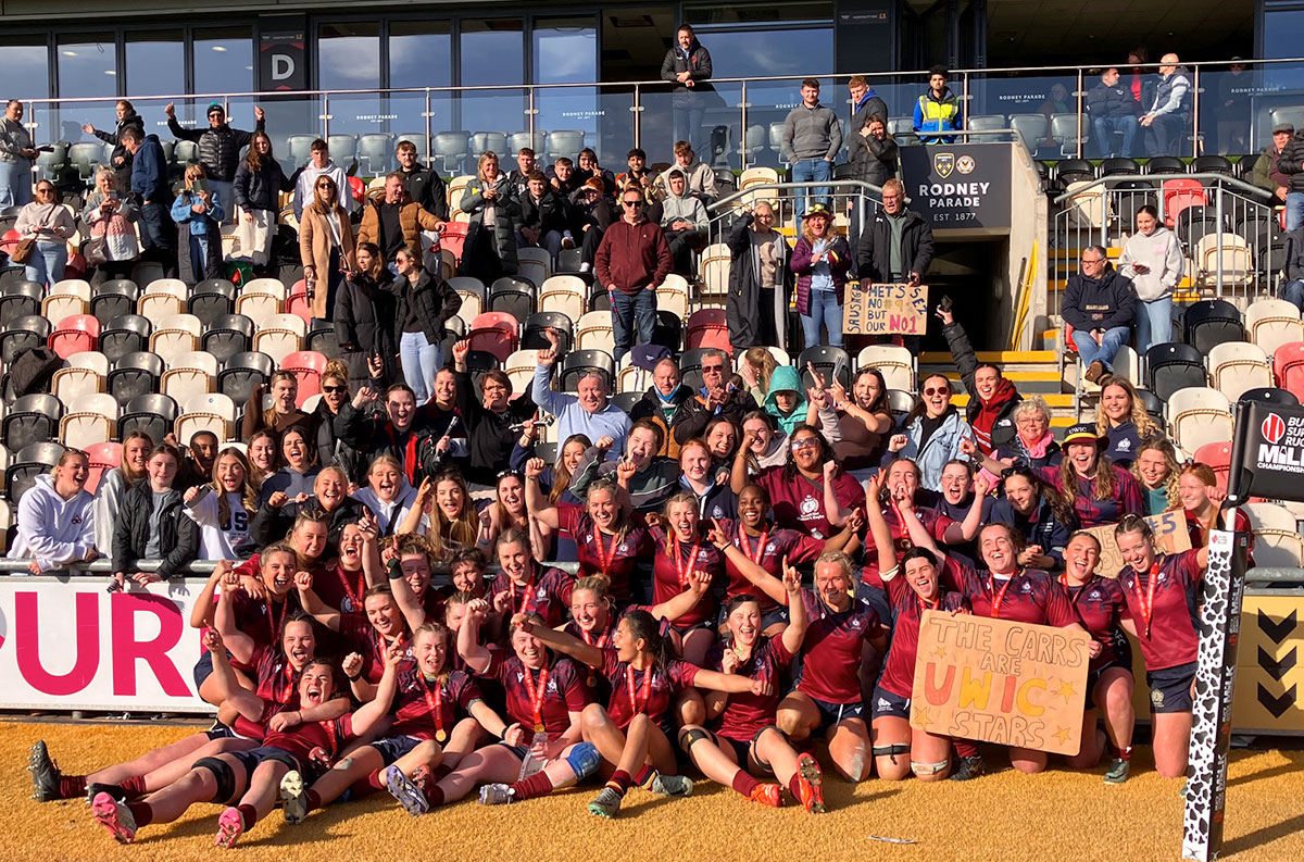 Women’s rugby team celebrating a championship win with fans in the stands at Rodney Parade stadium.