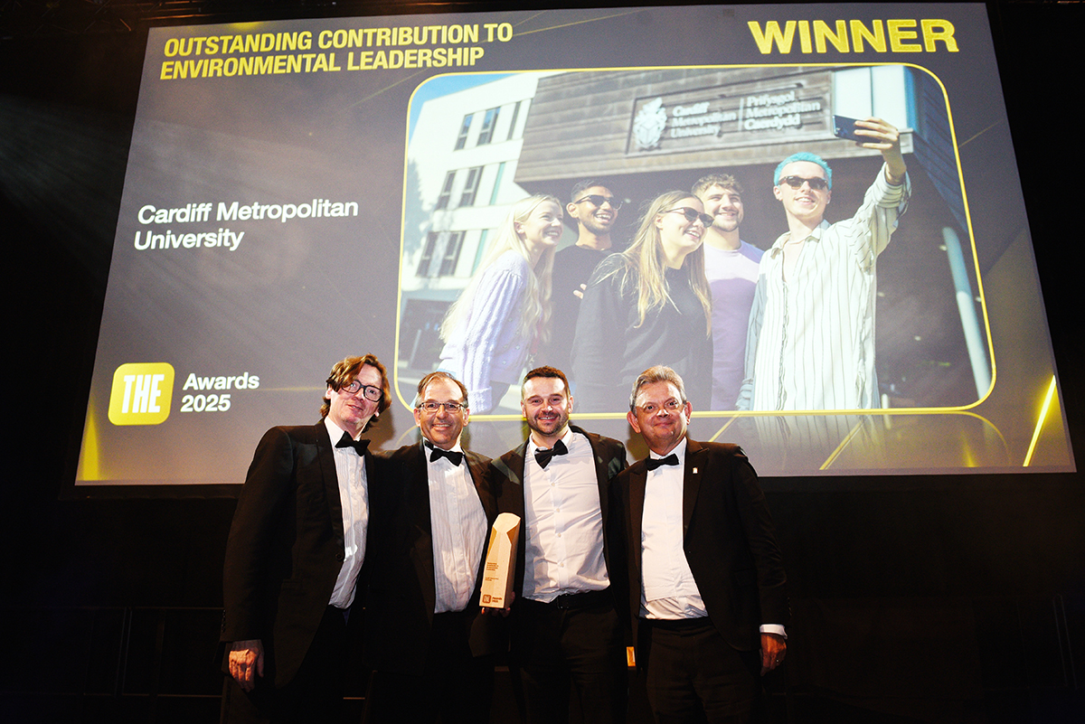 Cardiff Met staff accept an environmental leadership award on stage beneath a winner announcement screen.