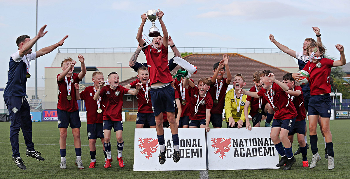 A group of young men joyfully holding up a trophy, celebrating winning a competition and enthusiasm for the sport.
