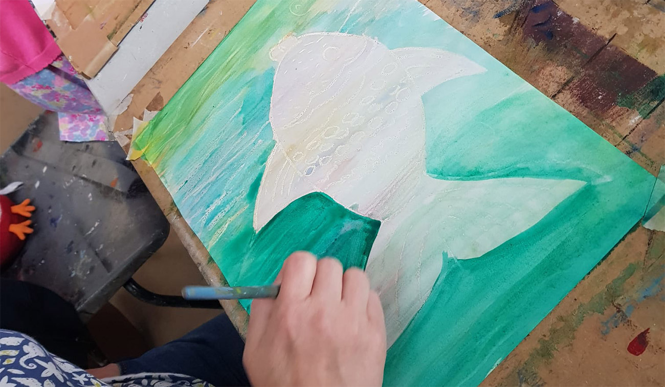 A woman paints a colorful fish on a sheet of paper, showcasing her artistic skills and creativity.