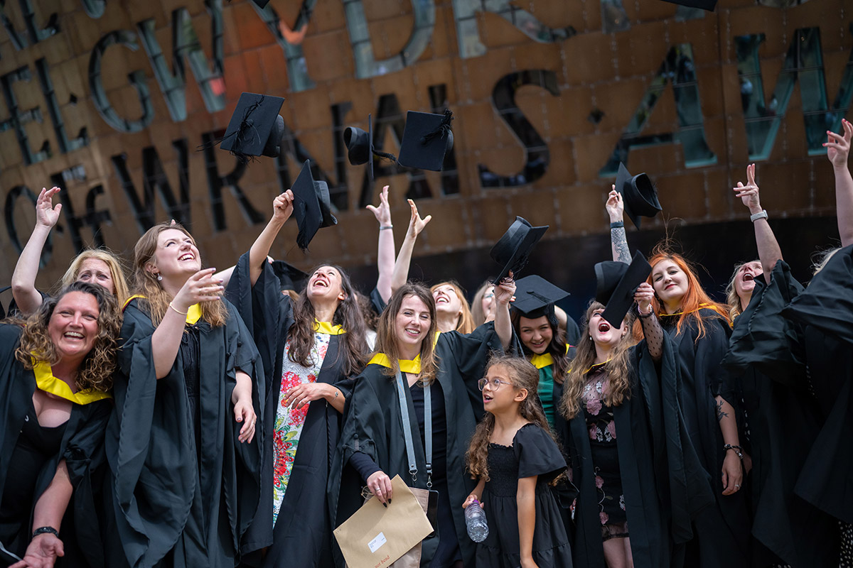 Graduates joyfully celebrate their graduation at the Wales National Stadium, surrounded by friends and family.
