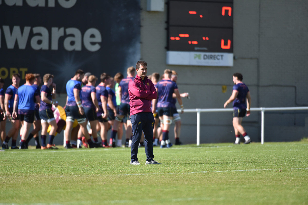 A rugby coach stands on the field with arms crossed, ready for coach, showcasing determination and focus.
