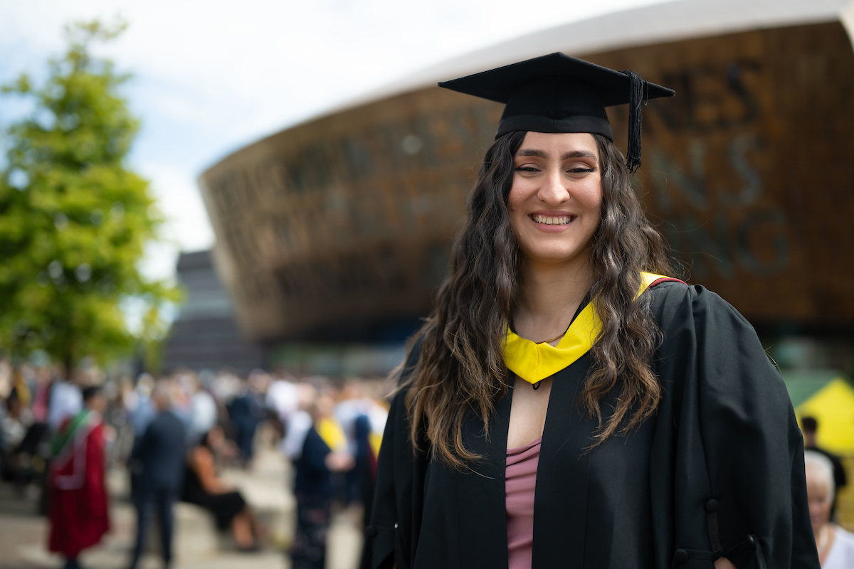 A woman wearing a graduation gown and mortarboard cap, smiling proudly at her graduation ceremony.