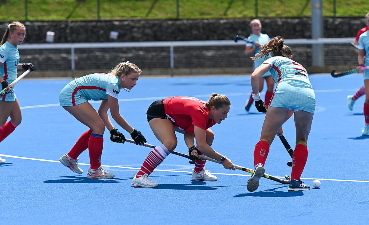 Women engaged in a field hockey match on a bright blue field, demonstrating skill and collaboration in the sport.