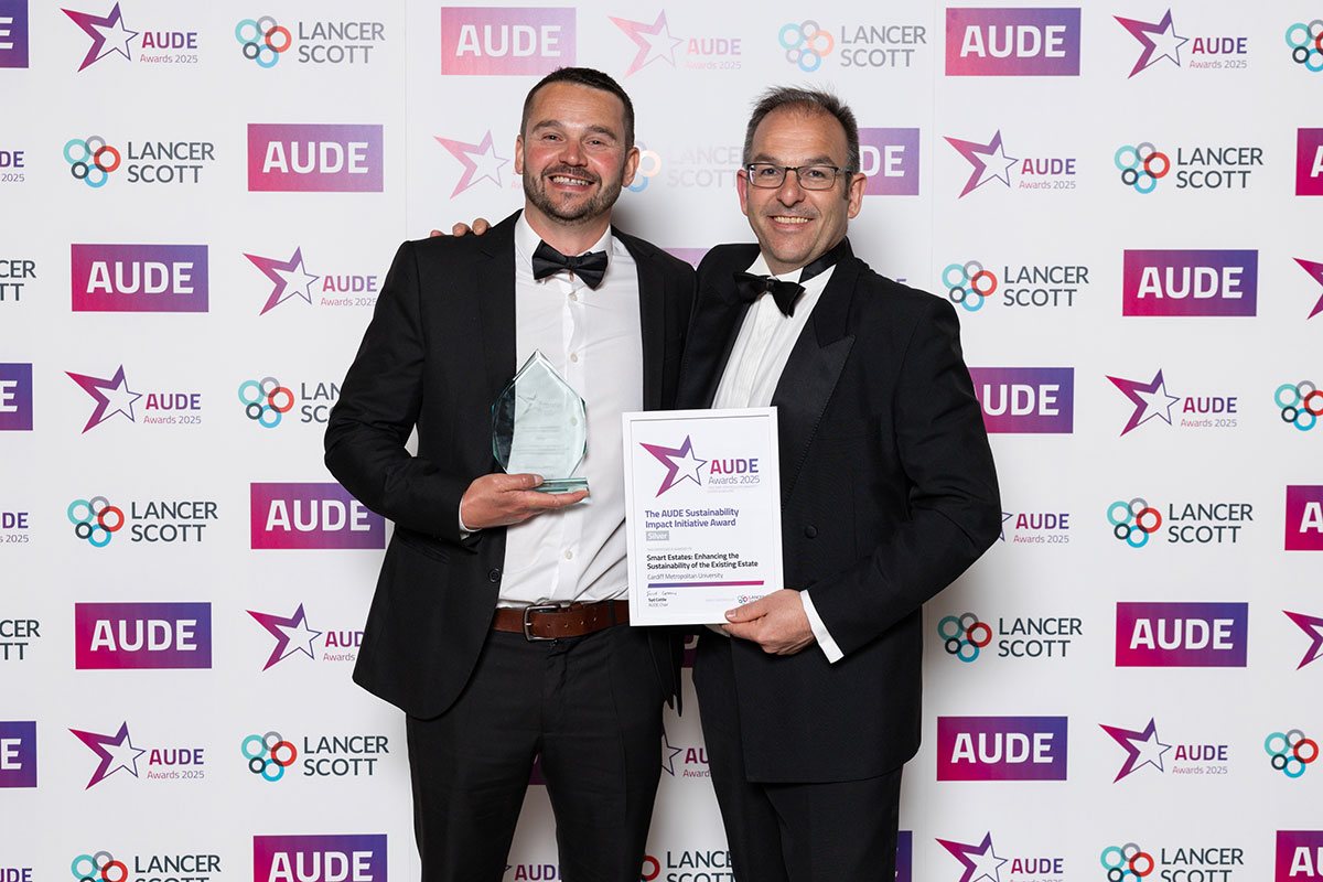 Two men in suits proudly hold an award in front of a decorative wall.