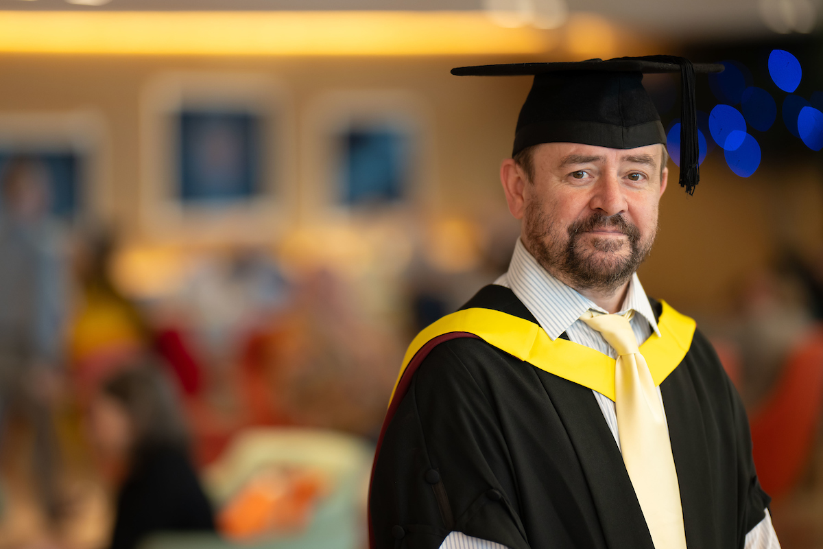 A man wearing a graduation gown and cap, celebrating his academic achievement with a proud smile.