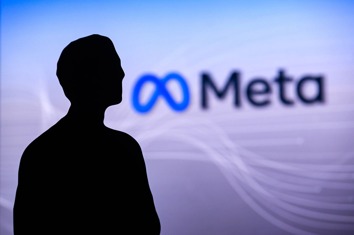 Silhouette of Mark Zuckerburg in front of a screen displaying the Meta logo, consisting of a blue infinity symbol and the word 