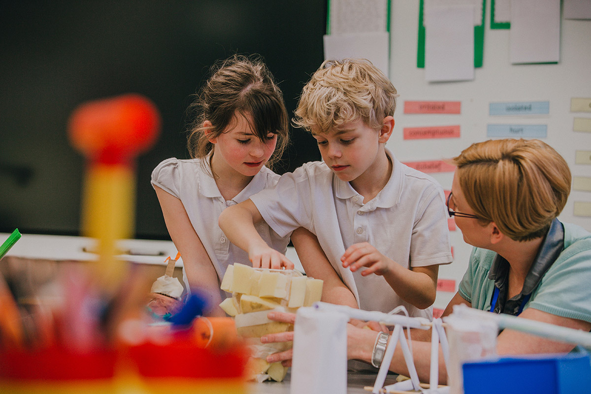 In a classroom, a teacher assists two children as they focus on a project, fostering teamwork and creativity.